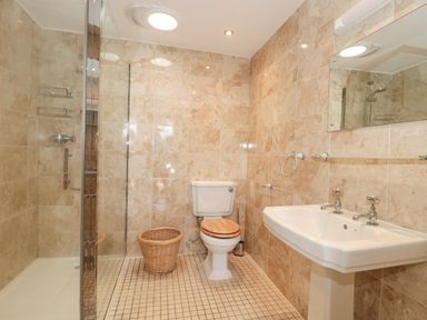 A bathroom with a shower cubicle toilet with wooden seat pedestal sink and a wicker basket at Orchard View in Redmary D Abitot near Hartpury