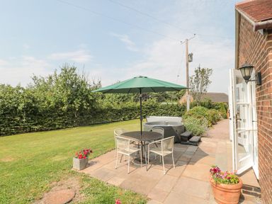 A garden patio with a round table and four chairs under a green umbrella and a hot tub next to a brick house at Orchard View Redmary D Abitot near Hartpury