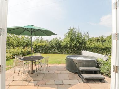 A patio with a table and chairs under a green umbrella and a hot tub with steps in a garden at Orchard View in Redmary D Abitot near Hartpury