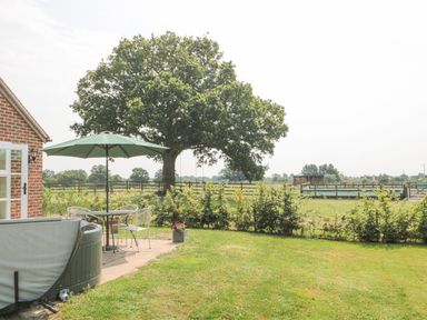 A backyard with a patio table and umbrella next to a hot tub and large tree at Orchard View in Redmary D'Abitot near Hartpury