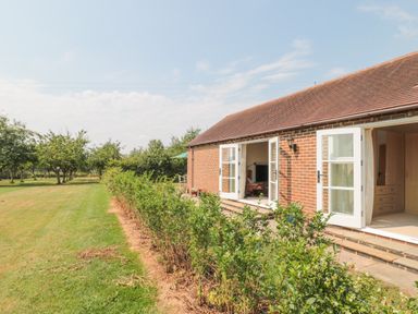 A garden with a lawn and shrubs next to a brick house with open white doors at Orchard View in Redmary DAbitot near Hartpury