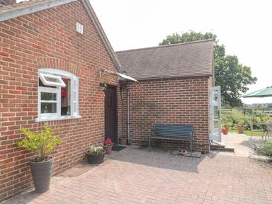A brick house exterior with potted plants a bench and open doors leading to a patio at Orchard View in Redmary D'Abitot near Hartpury