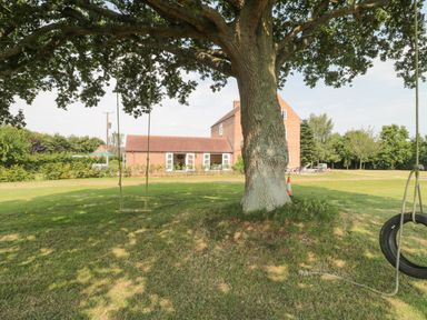 A large tree with two swings on a grassy lawn in front of a brick house at Orchard View in Redmary D Abitot near Hartpury