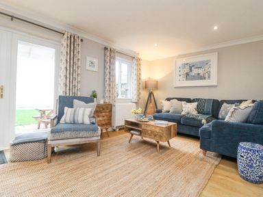 A living room with blue upholstered chairs and sofa wooden coffee table and floor lamp at Breeze Cottage in Falmouth