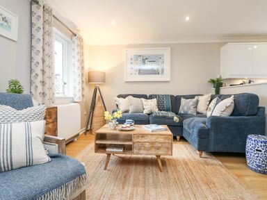 A living room with a blue sofa and armchair a wooden coffee table and a floor lamp at Breeze Cottage in Falmouth