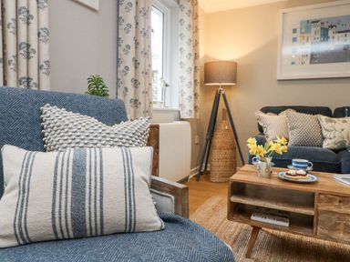 A living room with blue and white pillows on chairs table with flowers and tea set at Breeze Cottage in Falmouth