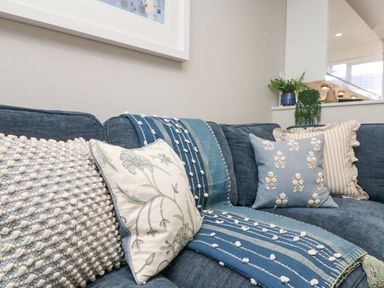 A blue sofa with four cushions and a blue patterned throw in a living room at Breeze Cottage in Falmouth