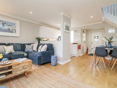 An open living room with a blue sectional sofa and wooden coffee table and a dining area with black chairs at Breeze Cottage in Falmouth