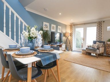 A dining table set with blue and white dishes next to a living room with a TV armchair and rug at Breeze Cottage in Falmouth