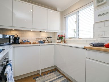 A kitchen with white cabinets a sink under a window and various kitchen items on the counters at Breeze Cottage in Falmouth