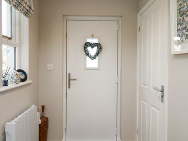 A hallway with a white door decorated with a heart-shaped wreath two white doors and a window with items on the windowsill at Breeze Cottage in Falmouth