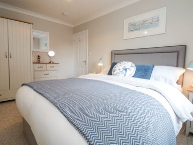A bedroom with a bed a wardrobe and a dresser with a mirror at Breeze Cottage in Falmouth