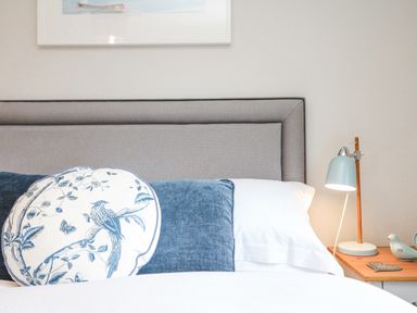 A bed with pillows and a bedside table with a lamp and decorative items at Breeze Cottage in Falmouth