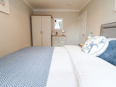 A bedroom with a bed, a wardrobe, a chest of drawers, a mirror, and a nightstand with a lamp at Breeze Cottage in Falmouth
