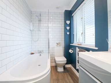 A bathroom with a bathtub shower toilet and sink with blue walls and white tiles at Breeze Cottage in Falmouth