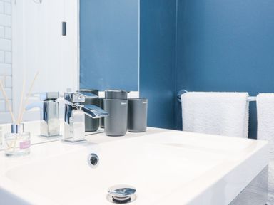 A bathroom sink with a chrome faucet black soap dispensers a lavender reed diffuser and white towels hanging on a towel rack against a blue wall at Breeze Cottage in Falmouth