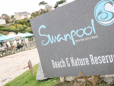 A large sign reading Swanpool Beach and Nature Reserve with outdoor seating and umbrellas in the background at Breeze Cottage in Falmouth