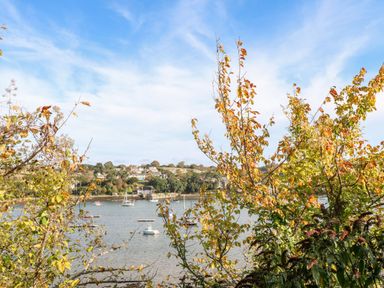 A river with boats and houses seen through trees with autumn leaves at Breeze Cottage in Falmouth