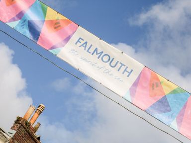A banner with colorful geometric shapes and the text FALMOUTH the spirit of the sea hanging outdoors with a blue sky background at Breeze Cottage in Falmouth