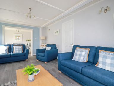 A living room with blue sofas a wooden coffee table with a plant and a lamp on a side table at Lowen Lodge in St Merryn near Padstow