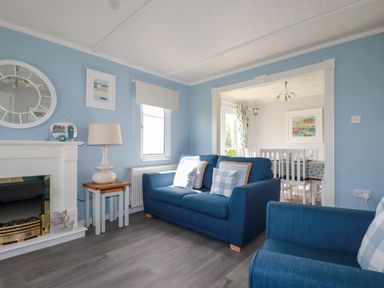 A living room with blue sofas a lamp side table and a fireplace leading to a dining room at Lowen Lodge St Merryn near Padstow