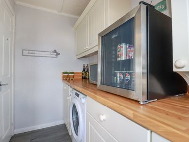 A kitchen with a washing machine countertop mini fridge microwave and wall cabinets at Lowen Lodge in St Merryn near Padstow