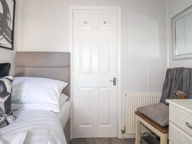 A bedroom with a bed, pillows, a white door, a chair with cushions, and a radiator at Lowen Lodge in St Merryn near Padstow