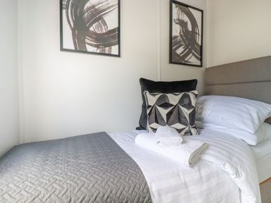 A bedroom with a bed made with white and gray bedding and two framed abstract paintings on the wall at Lowen Lodge in St Merryn near Padstow