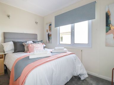 A bedroom with a bed with pillows and folded towels under a window at Lowen Lodge in St Merryn near Padstow