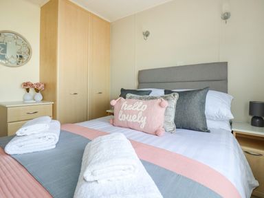 A bedroom with a bed with pillows and towels and a wardrobe and bedside tables at Lowen Lodge in St Merryn near Padstow