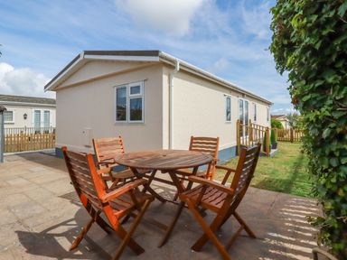 An outdoor patio with a round wooden table and four wooden chairs next to a beige mobile home at Lowen Lodge in St Merryn near Padstow