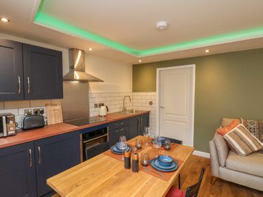 A kitchen and dining area with blue cabinets a wooden table set for four and a beige sofa with cushions at Picadore Two in Scarborough