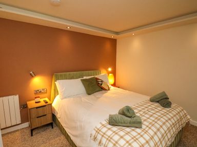 A bedroom with a double bed green headboard bedside tables and rolled towels at Picadore Two in Scarborough