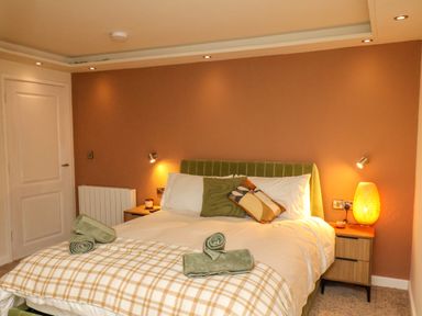 A bedroom with a bed with pillows and folded towels a bedside table with a lamp and a door at Picadore Two in Scarborough