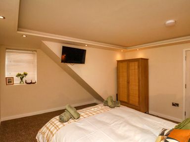 A bedroom with a bed, wooden wardrobe, wall-mounted TV, window with blinds and flowers at Picadore Two in Scarborough