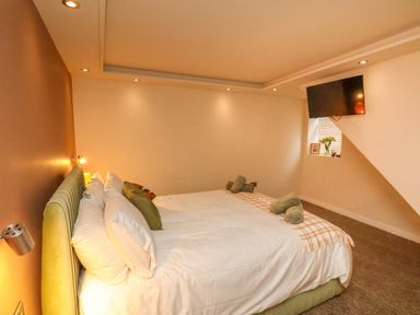 A bedroom with a bed with white sheets and green pillows a wall mounted television and a small window with flowers at Picadore Two in Scarborough