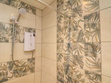 A shower with a handheld showerhead and a water heater unit on tiled walls with leafy patterns at Picadore Two in Scarborough