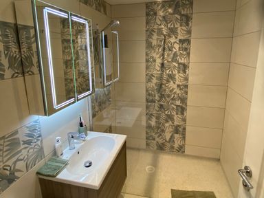 A bathroom with a sink vanity unit mirror with lights and a walk in shower with patterned tiles at Picadore Two in Scarborough