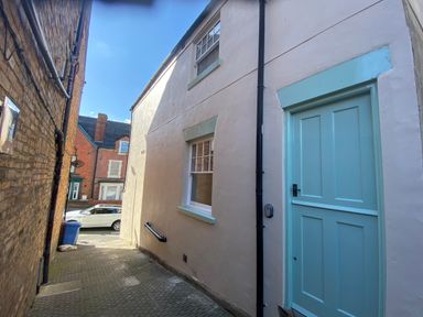 An alleyway with a tan building on the right featuring a blue door and window and a narrow brick building on the left at Picadore Two in Scarborough