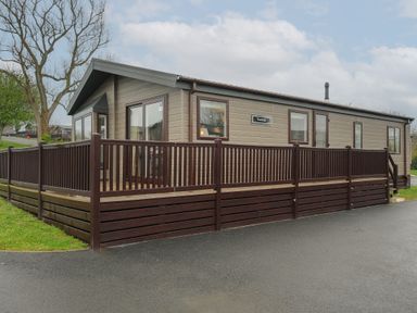A single story park home with brown wooden deck railings and multiple windows at Lodge 74 at Riviera Bay Coastal Retreat Brixham