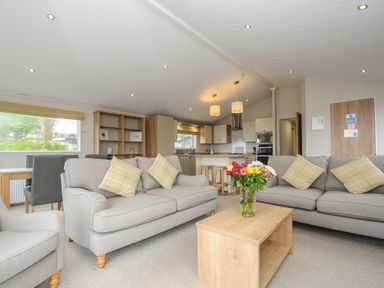 A living room with sofas a wooden coffee table with flowers a dining table and a kitchen area at Lodge 74 at Riviera Bay Coastal Retreat in Brixham