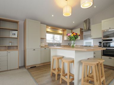 A kitchen with wooden stools around an island and cabinets with a vase of flowers on the island at Lodge 74 at Riviera Bay Coastal Retreat in Brixham
