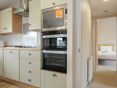 A kitchen with oven microwave stove and cabinets next to a hallway leading to a bedroom at Lodge 74 at Riviera Bay Coastal Retreat in Brixham