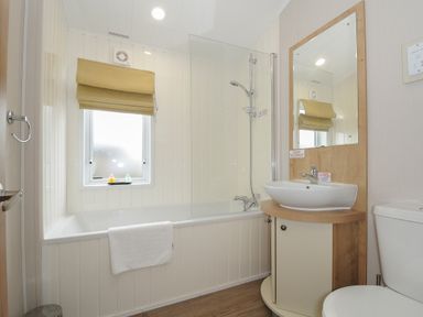 A bathroom with a bathtub shower combination a window with a blind a sink with a mirror and a toilet at Lodge 74 at Riviera Bay Coastal Retreat in Brixham