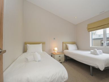 A bedroom with two single beds with white linens and a nightstand with a lamp between them at Lodge 74 at Riviera Bay Coastal Retreat in Brixham