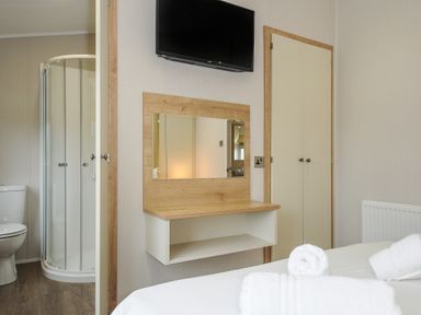 A bedroom with a bed and towels with a wall-mounted tv mirror a closet and an adjoining bathroom with a shower at Lodge 74 at Riviera Bay Coastal Retreat Brixham