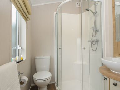 A bathroom with a toilet, shower with glass doors, a sink on a wooden countertop, and a window with a beige blind at Lodge 74 at Riviera Bay Coastal Retreat in Brixham