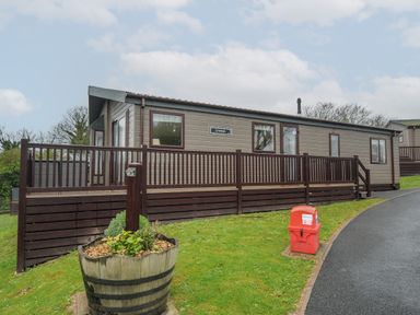 A mobile home with brown railing on a grassy slope near a road at Lodge 58 at Riviera Bay Coastal Retreat in Brixham