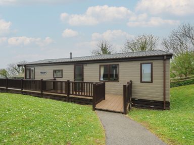 A single story mobile home with a wooden ramp and railing surrounded by grass at Lodge 59 at Riviera Bay Coastal Retreat in Brixham