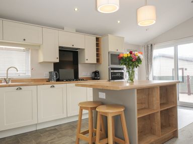 A kitchen with wooden stools and a flower vase on the island at Lodge 59 at Riviera Bay Coastal Retreat in Brixham